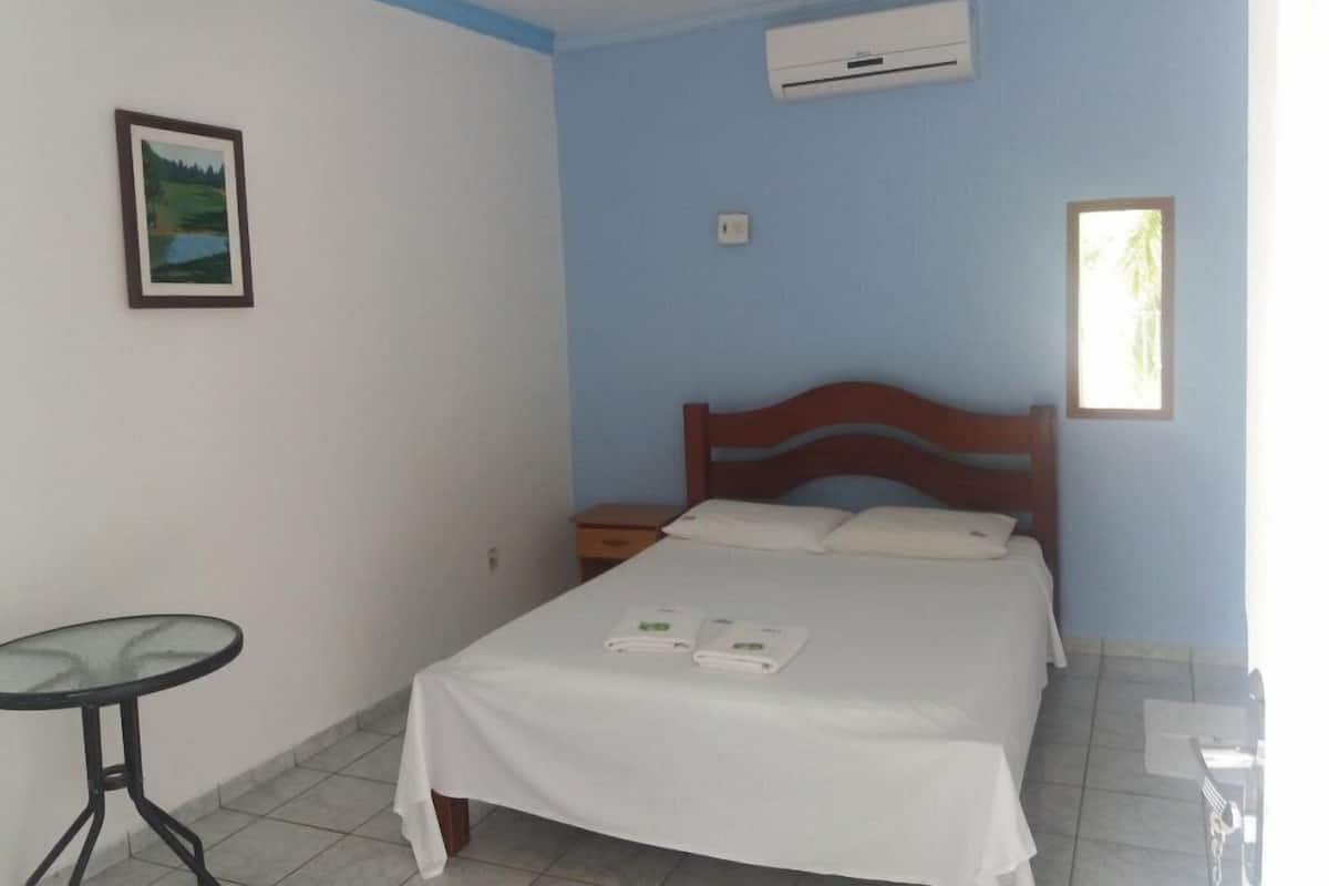 Una habitación con cama, una mesita y un equipo de aire acondicionado.