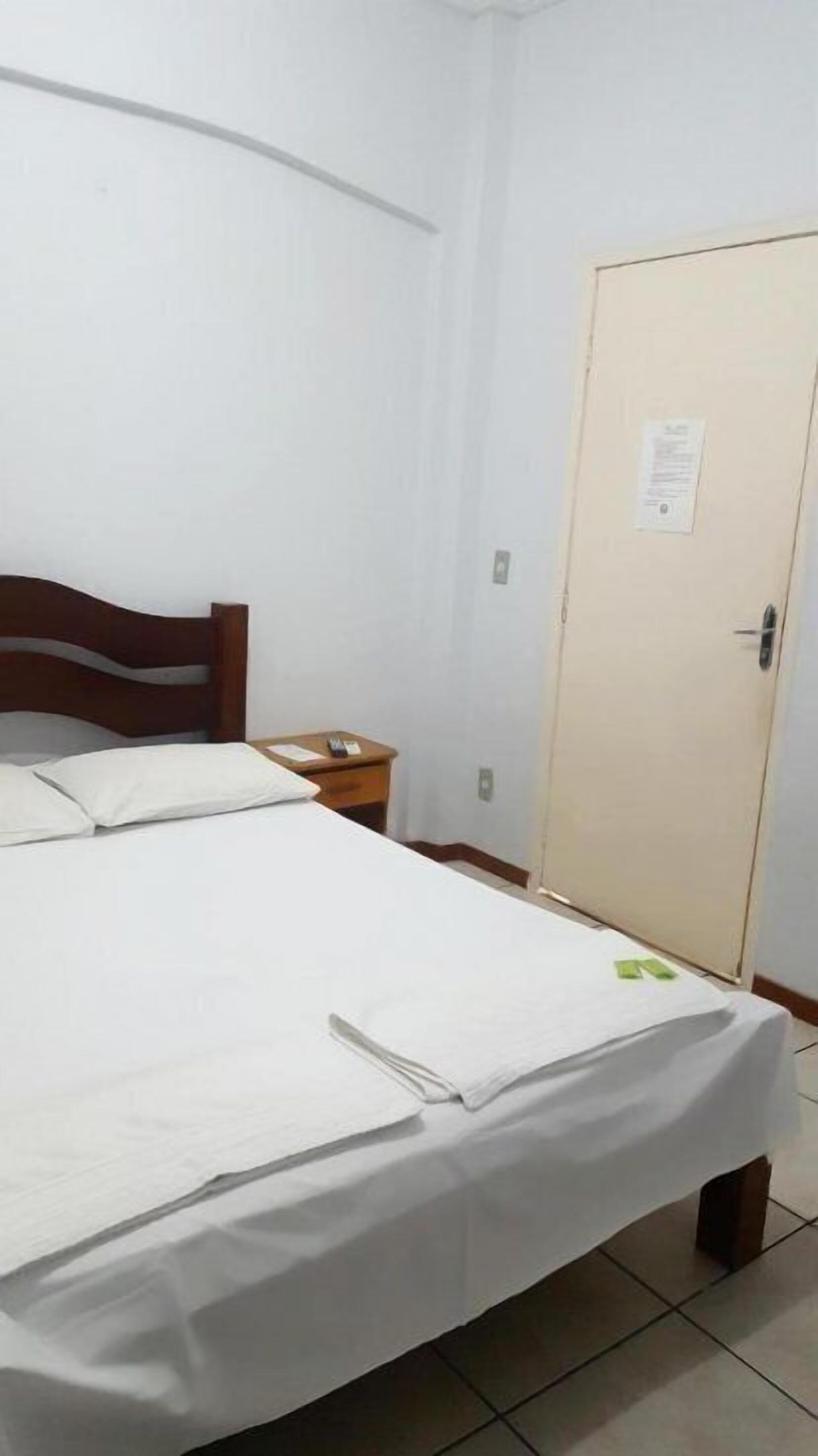 A single-bed room with a wooden headboard, a bedside table with a lamp, and a door with a notice on it.