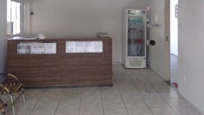 A reception area with a wooden counter, a refrigerator, and a tiled floor. - Ami Hotel (Varzea Grande)