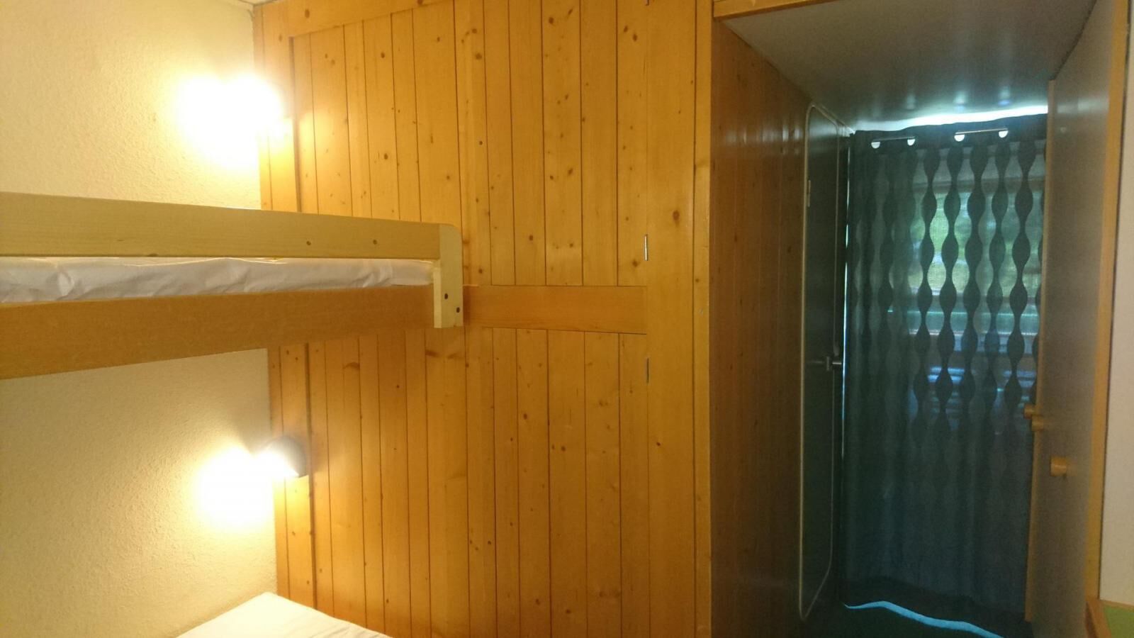 Une pièce aux murs en bois, avec un lit superposé et une porte donnant sur une autre pièce.