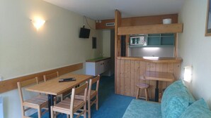 Eine kleine Küche mit einer Mikrowelle, einem Holztisch mit Stühlen und einem kleinen Hocker.