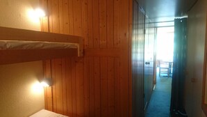 Ein Zimmer mit Holzwänden, einem Etagenbett, einer Tür zu einem anderen Raum und einem Fenster.