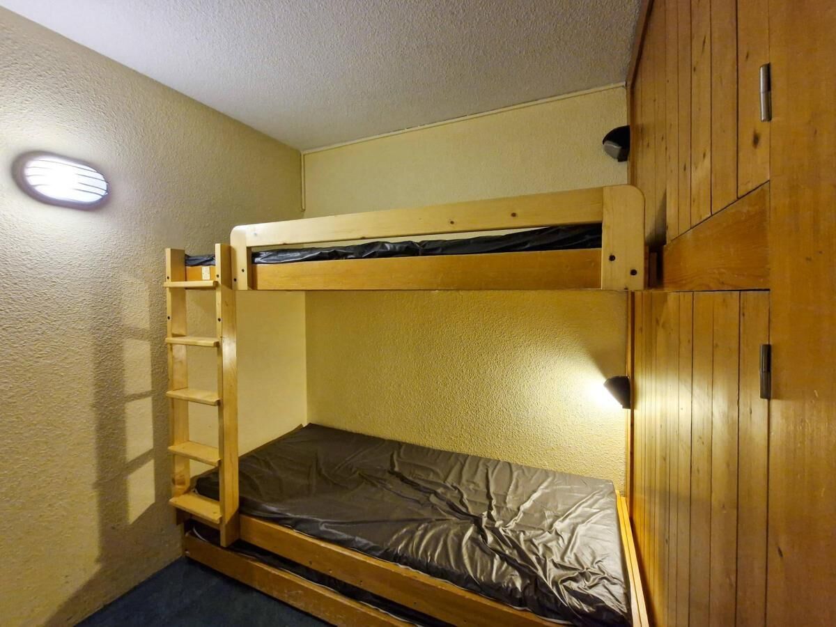 Een stapelbed met een ladder, een houten garderobe en een klein raam.
