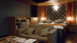 A compact hotel room with a bed, a sofa, a small table with magazines, and a kitchenette area. - Hotel Marion (Suzuka)