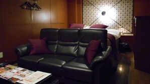 A room with a black leather sofa, a small table with magazines, and a patterned wallpaper. - Hotel Marion (Suzuka)