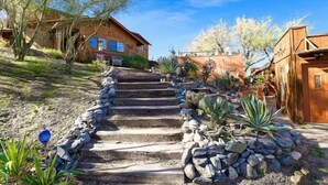 Eine Holztreppe führt zu einem Haus mit Steinbord und Wüstenpflanzen.