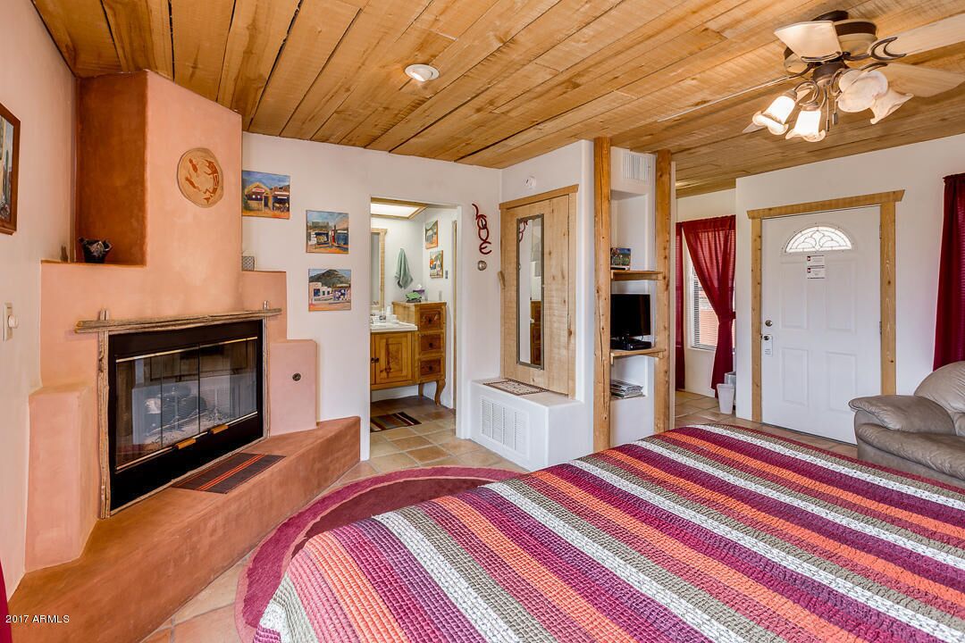Un dormitorio acogedor con chimenea, una cama con manta de rayas coloridas, techo de madera y una puerta que da a otra habitación.