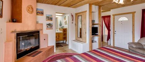 Un dormitorio acogedor con chimenea, una cama con manta de rayas coloridas, techo de madera y una puerta que da a otra habitación.