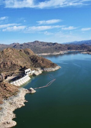 A dam with a small building on a rocky outcrop, a calm lake, and distant mountains.
