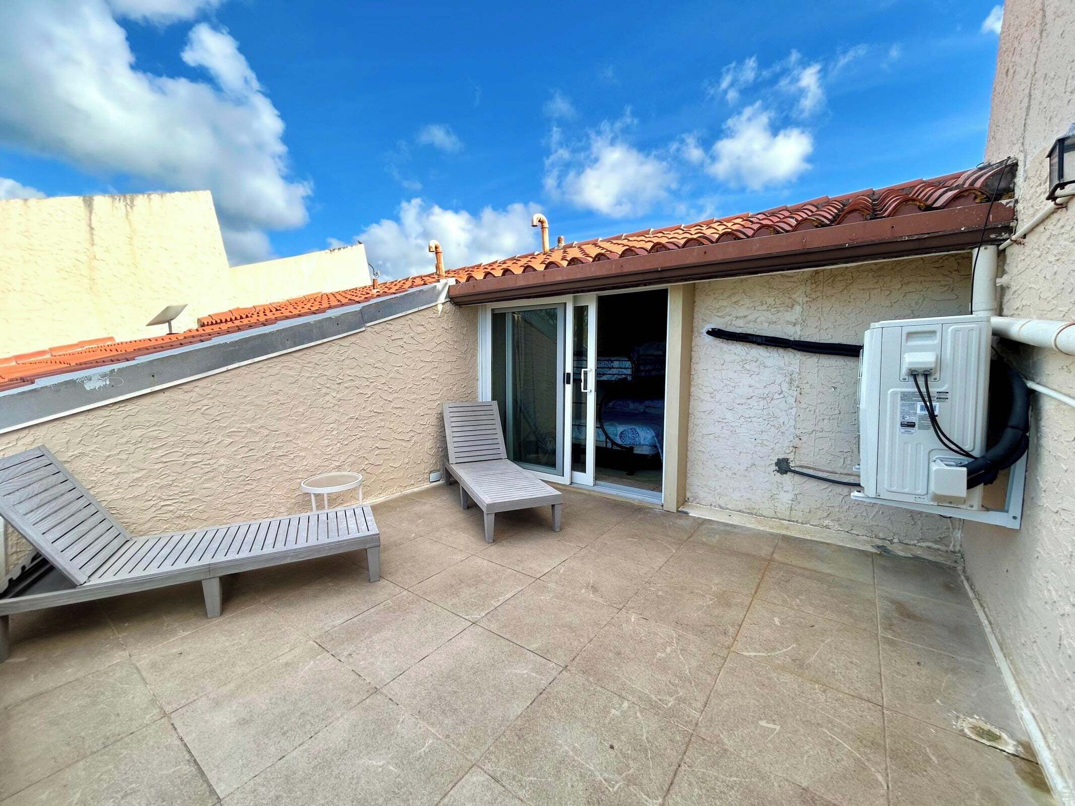A small outdoor patio with two lounge chairs, a table, and a sliding glass door leading to a bedroom.