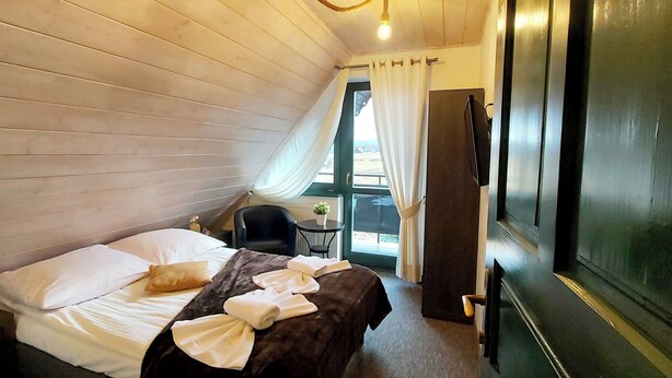 Ein Zimmer mit einem Bett, einem Sessel, einem kleinen Tisch mit Pflanze und einem Fernseher an der Wand.