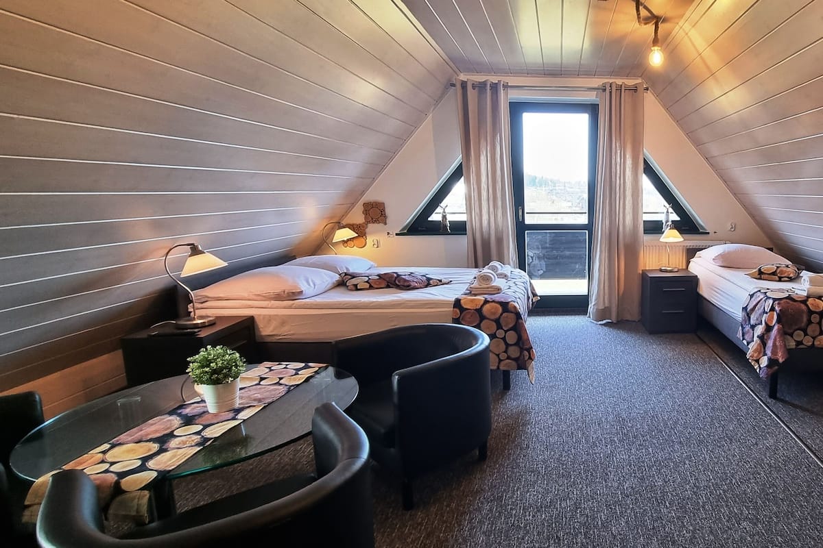 A cozy attic bedroom with two beds, a dining table, and a TV.