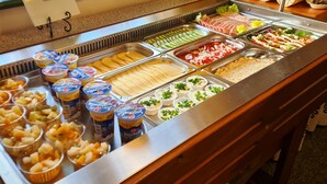 Ein Buffet mit verschiedenen Speisen, darunter Obst, Joghurt und Aufschnitt.