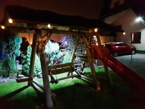 A playground with a slide and swings, a red car parked nearby, and a house in the background. - Gościniec Na Brzyzku (Bukowina Tatrzanska)