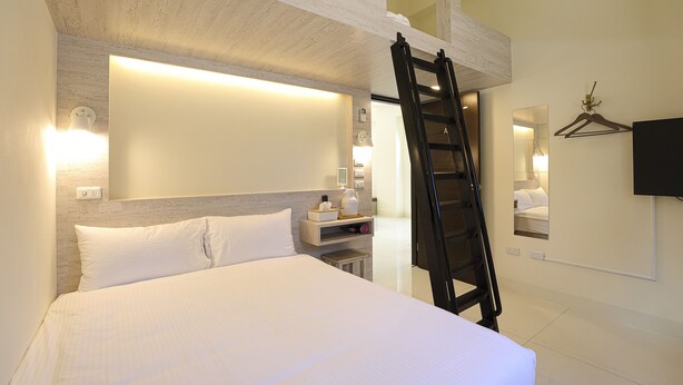 Una habitación de hotel con una cama, una mesita de noche, un televisor de pared y una escalera de madera.