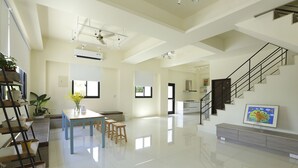 Un amplio salón con una escalera, una mesa de comedor y un televisor montado en la pared.