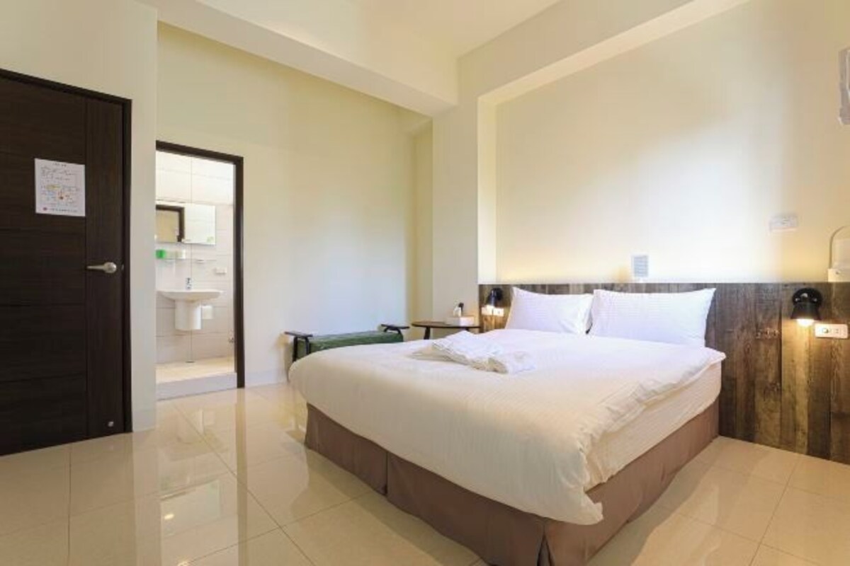 A hotel room with a large bed, a bedside table, a lamp, and a view of the bathroom.
