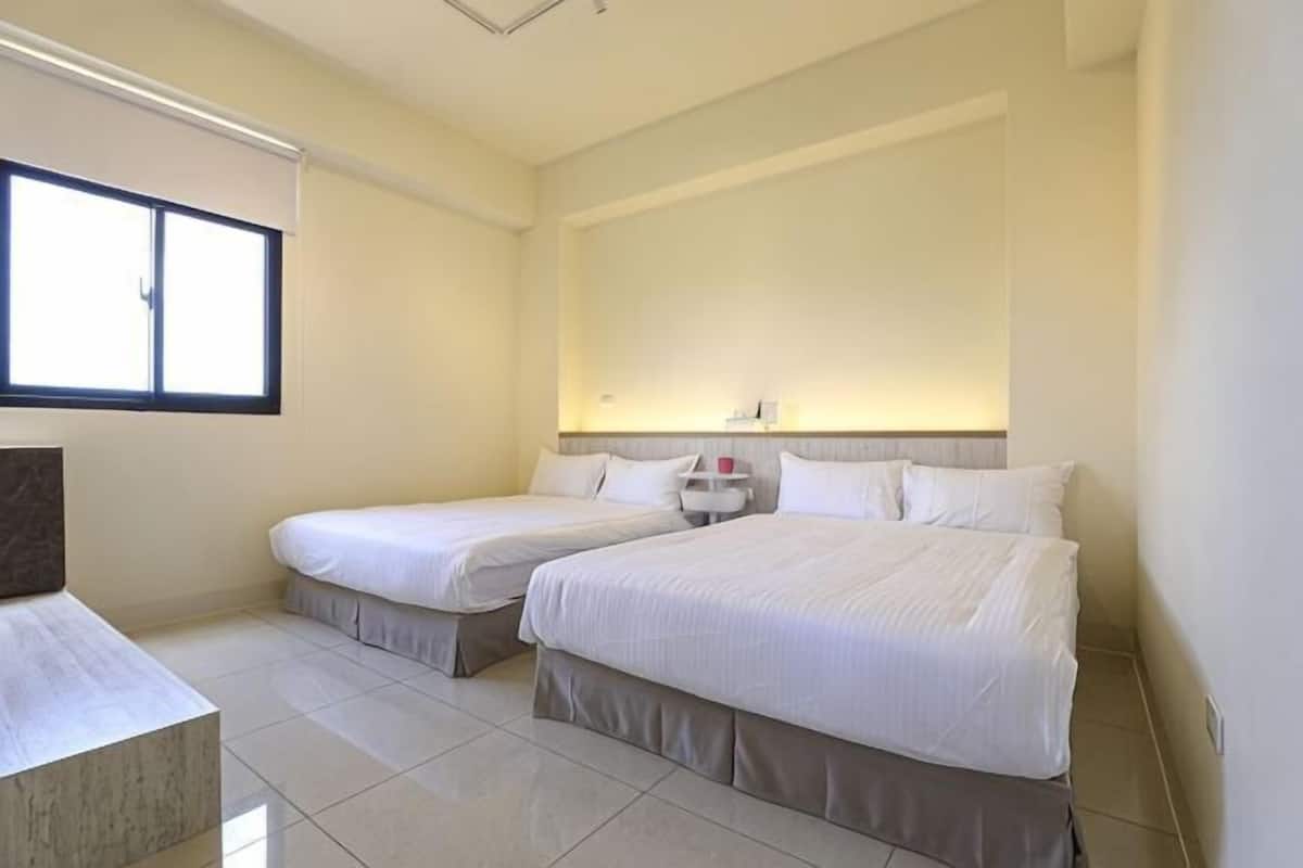 Quarto de hotel com duas camas, mesa de cabeceira e janela.