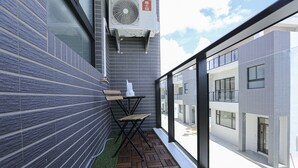 Fachada de un edificio moderno con un muro de azulejos, suelo de madera y una pequeña mesa con una silla.