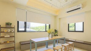 Una habitación luminosa con una mesa grande, dos taburetes, un estante con objetos y un ventanal con vistas.