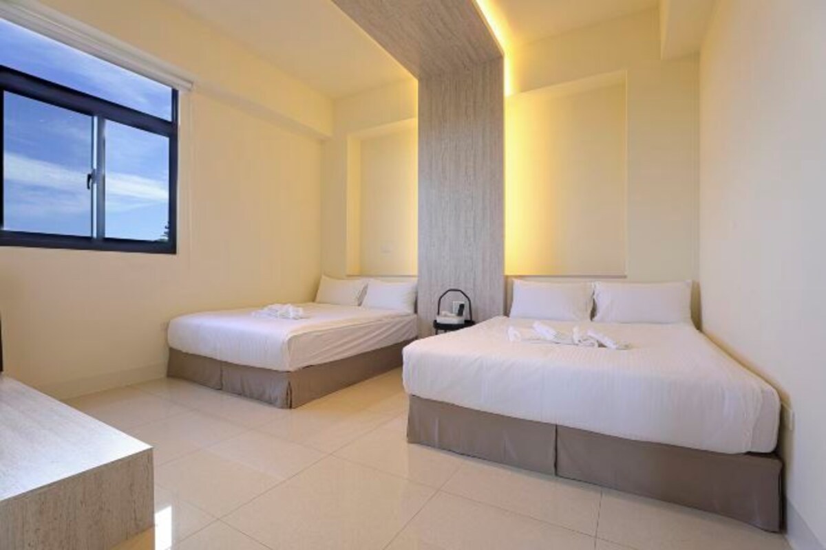A hotel room with two beds, a large window, and a modern design.
