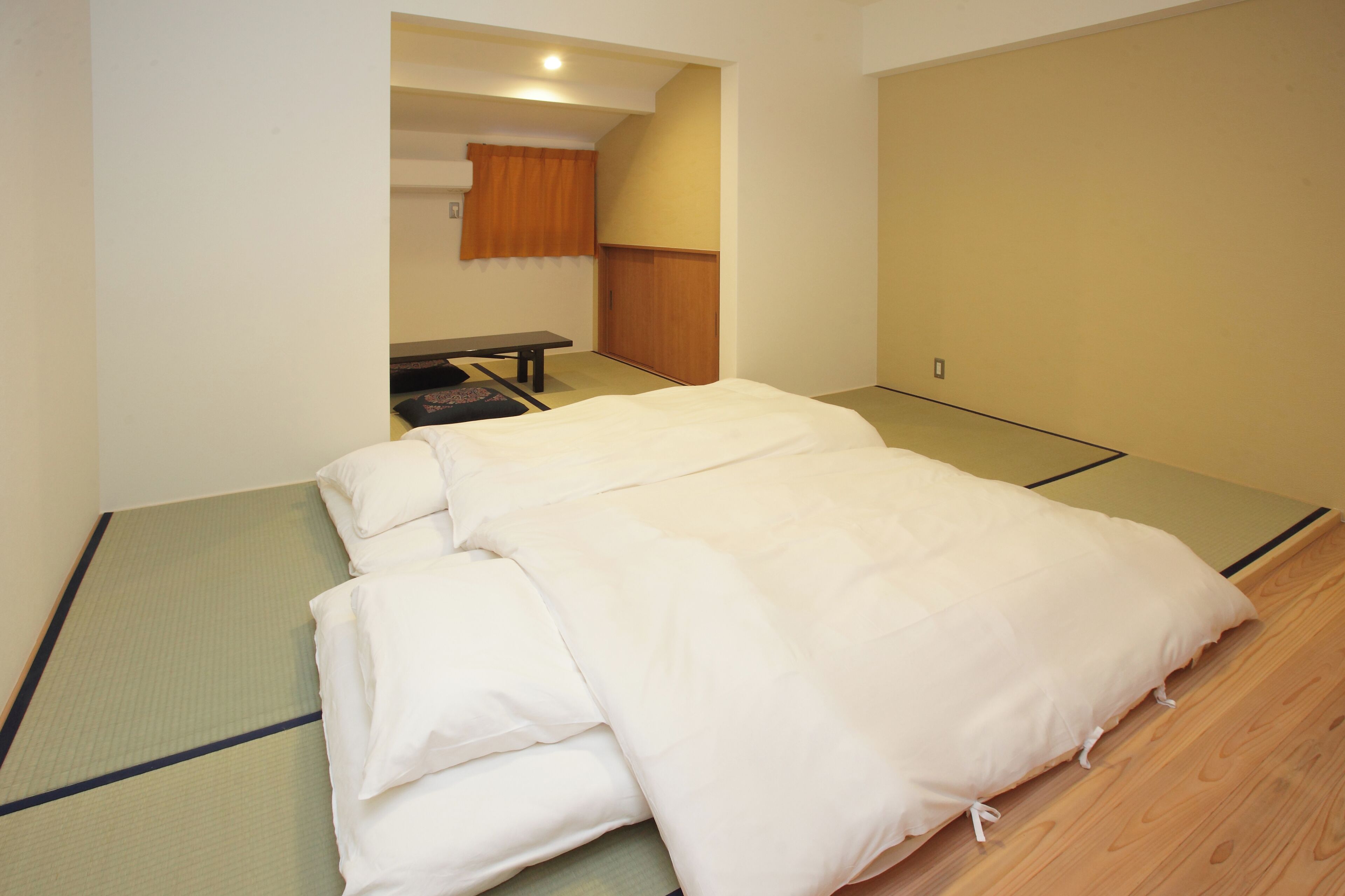 A room with a tatami mat floor, a bed with white bedding, a wooden wardrobe, and a small table with a bench.