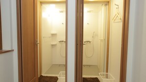Un pasillo con dos puertas que dan a un baño. El baño tiene ducha, inodoro y un pequeño espacio de almacenamiento.