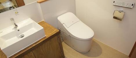 Un baño con lavamanos blanco, mueble de madera, inodoro blanco y un dispensador de papel higiénico montado en la pared.