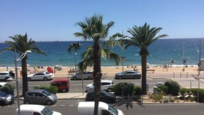 Une vue sur la plage, avec des voitures garées, des palmiers et un ciel bleu dégagé.
