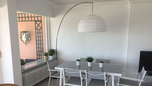 Un coin repas avec une table et des chaises blanches, un luminaire suspendu et des plantes en pot.