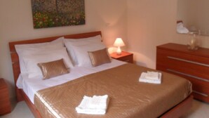 Een hotelkamer met een bed, een nachtkastje met een lamp, een kast en een schilderij aan de muur.