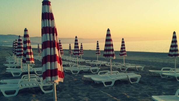 Een strand met rijen witte ligbedden en gestreepte strandparasols.