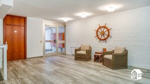 A spacious living area with a wooden door, a glass door leading to a storage room, wicker chairs, and a ship's wheel decoration on the wall. - App. with elevator + gr. Balcony + WLAN + 2 bicycles + beach chair package possible (Travemünde)