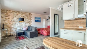 A modern living room with a stone wall, grey sofa, red bed, and a wooden dining table. - App. with elevator + gr. Balcony + WLAN + 2 bicycles + beach chair package possible (Travemünde)