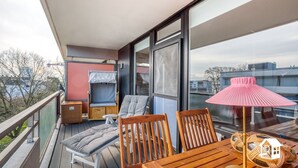 A balcony with a wooden table, two chairs, a small sofa, and a pink lamp. - App. with elevator + gr. Balcony + WLAN + 2 bicycles + beach chair package possible (Travemünde)