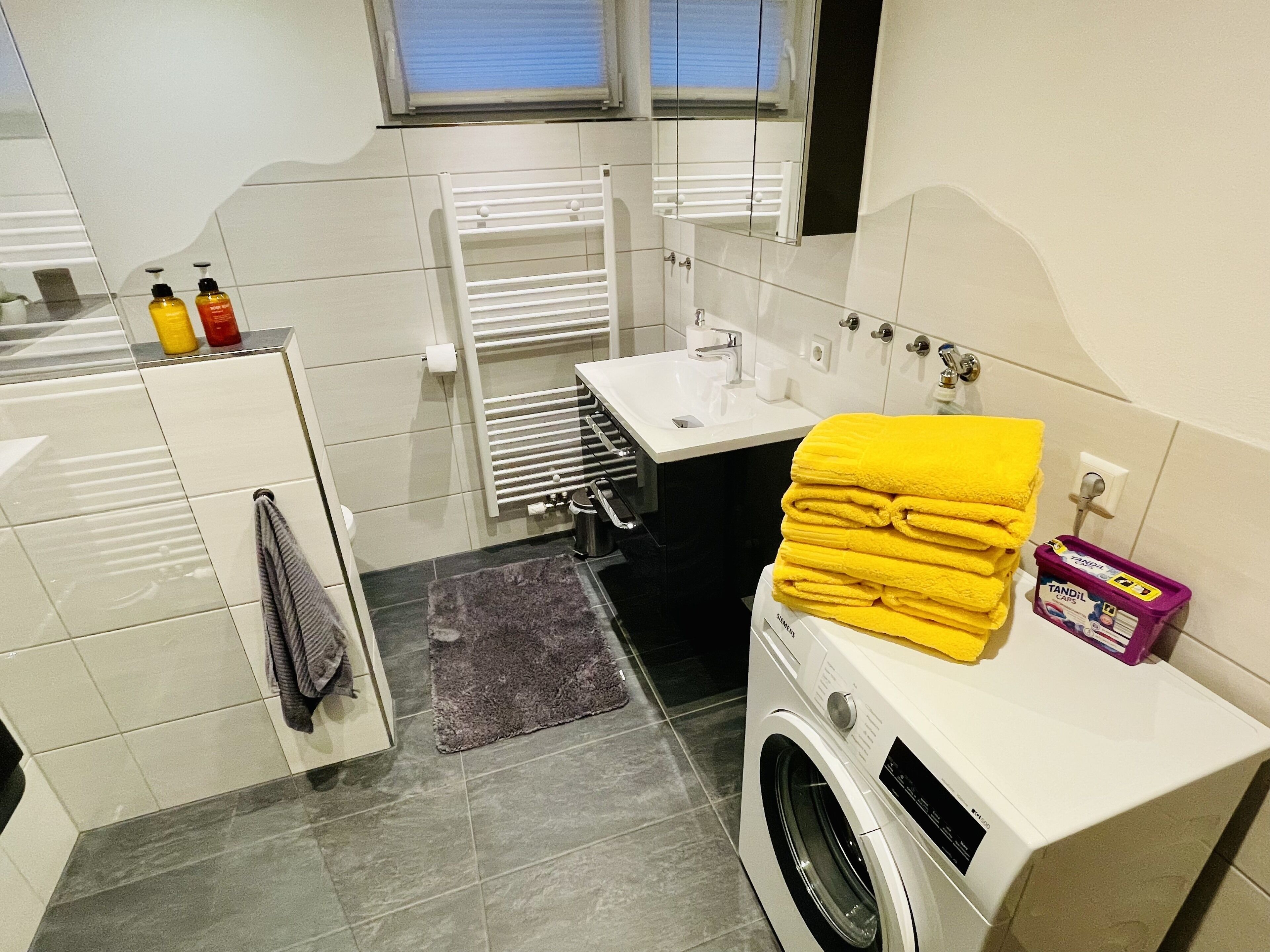 Un baño moderno con lavadora, lavamanos y perchero.