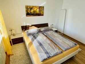 Une chambre bien rangée, avec un lit, une table de chevet, une lampe et un tableau accroché au mur.