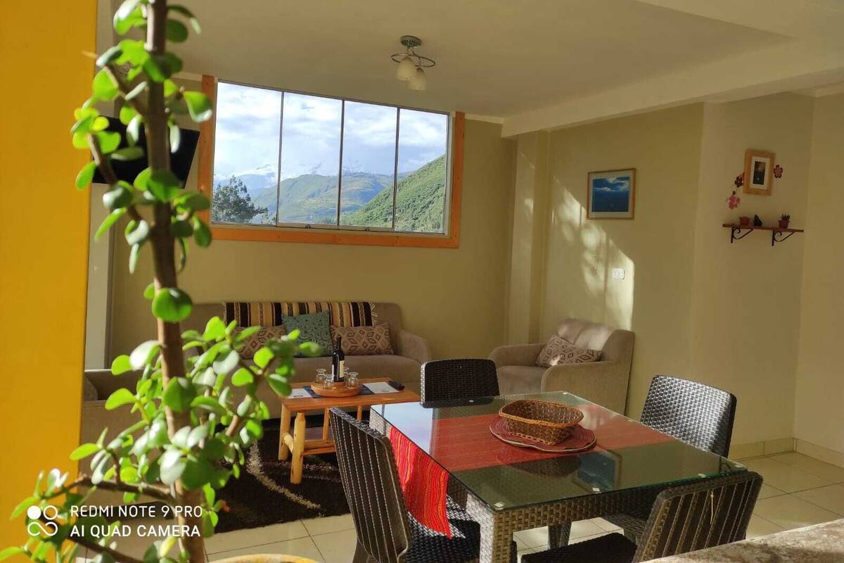 A living room with a sofa, a glass-top dining table, and a view of mountains through a large window.
