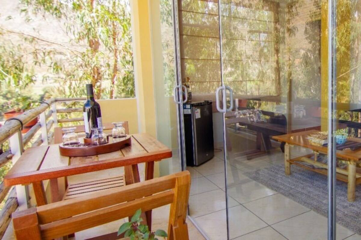 A glass-enclosed room with a dining area, a sofa, and a small table with a bottle and glasses.