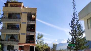 Un edificio de varios pisos con balcones, una señal de calle y una montaña al fondo.