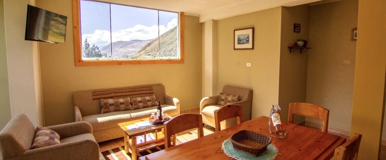 A cozy living room with a wooden dining table, two sofas, and a large window with a mountain view.