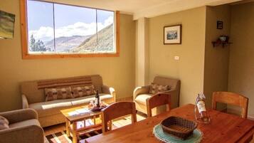 A cozy living room with a wooden dining table, two sofas, and a large window with a mountain view.