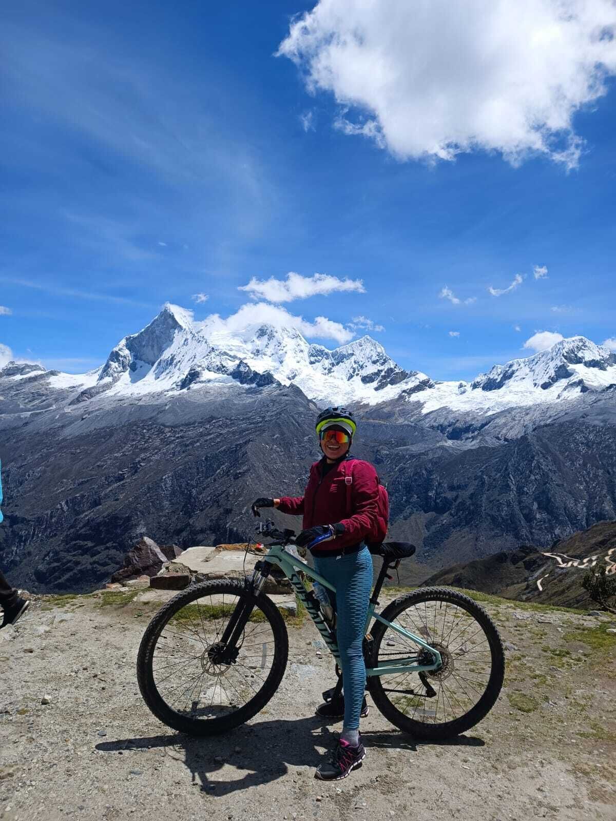 A person standing next to a mountain bike on a rocky terrain with snow-capped mountains in the background.