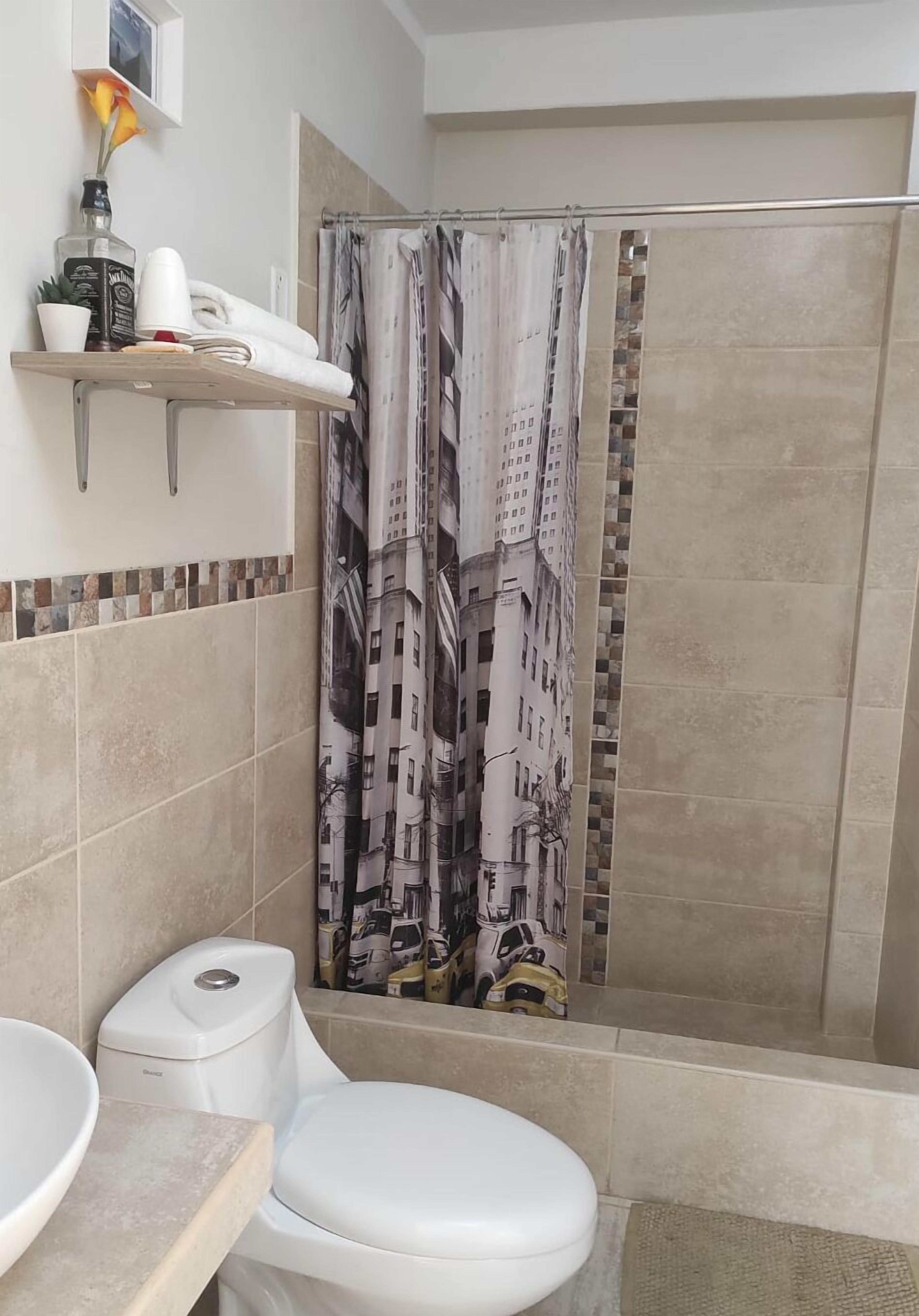 Een badkamer met toilet, wastafel, douchegordijn met stadsgezicht en een plank met toiletartikelen.
