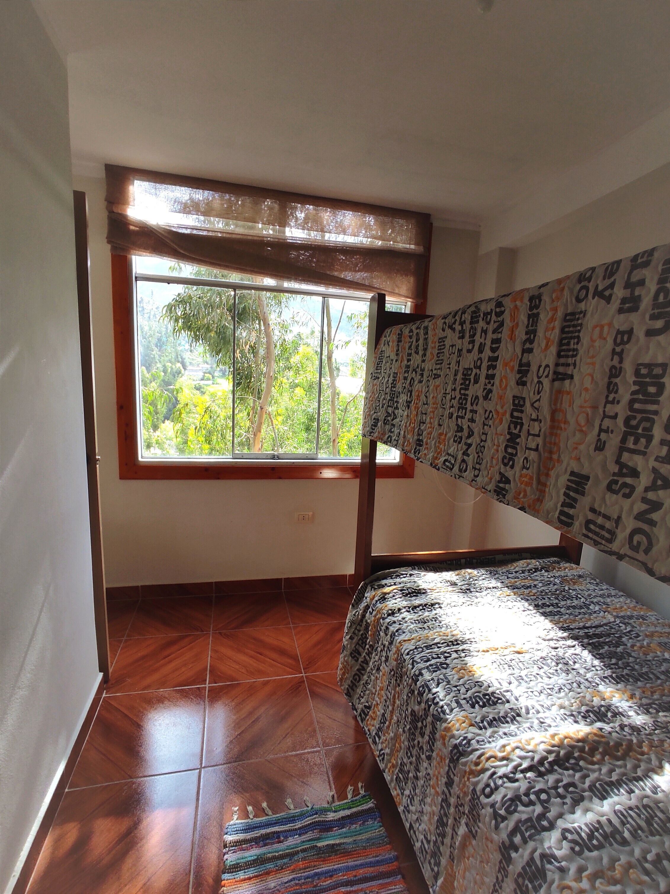 A room with a bunk bed, a window with a view of greenery, and a tiled floor.