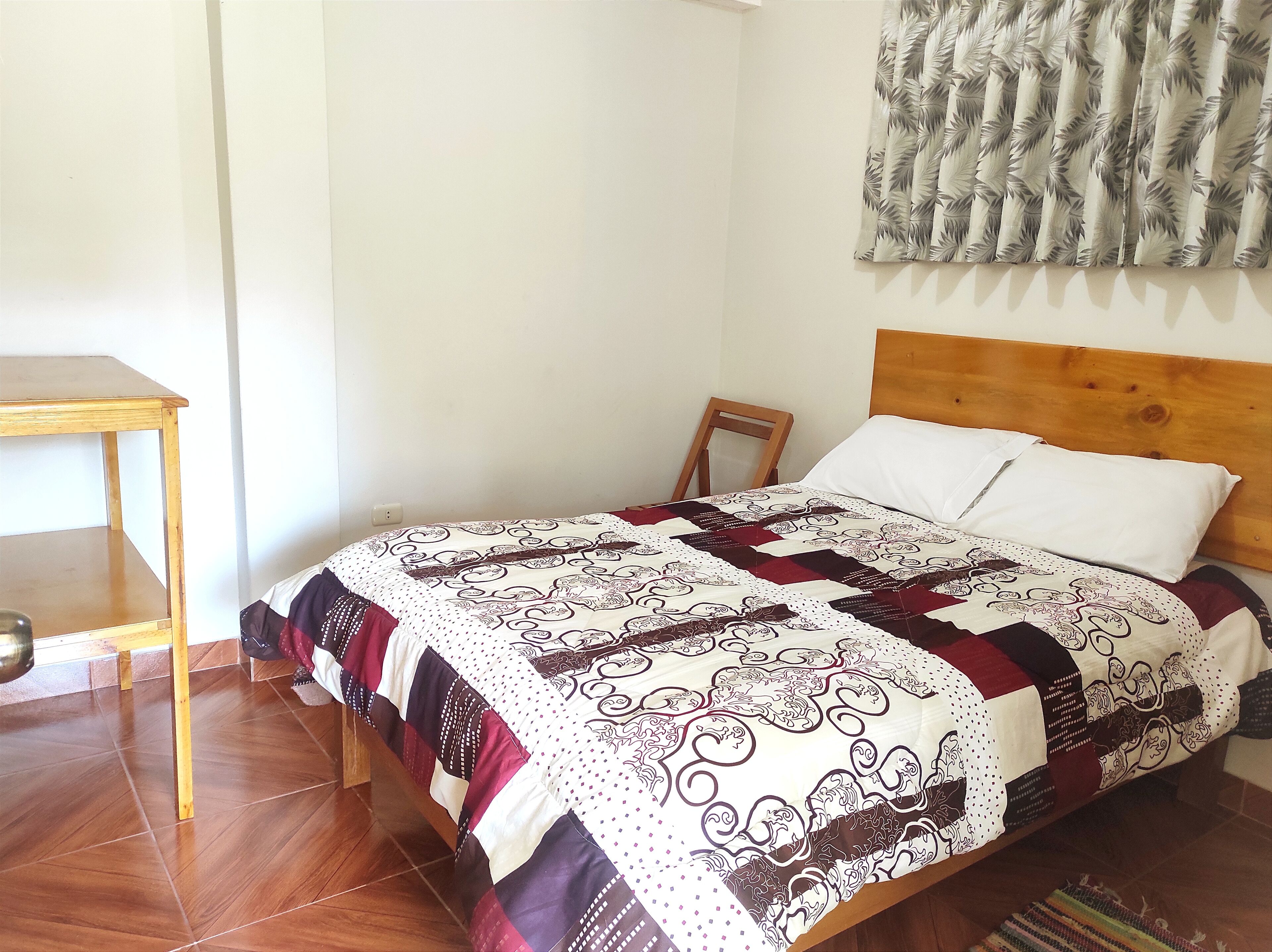 A bedroom with a wooden bed, a white pillow, a patterned quilt, a wooden nightstand, and a small wooden chair.