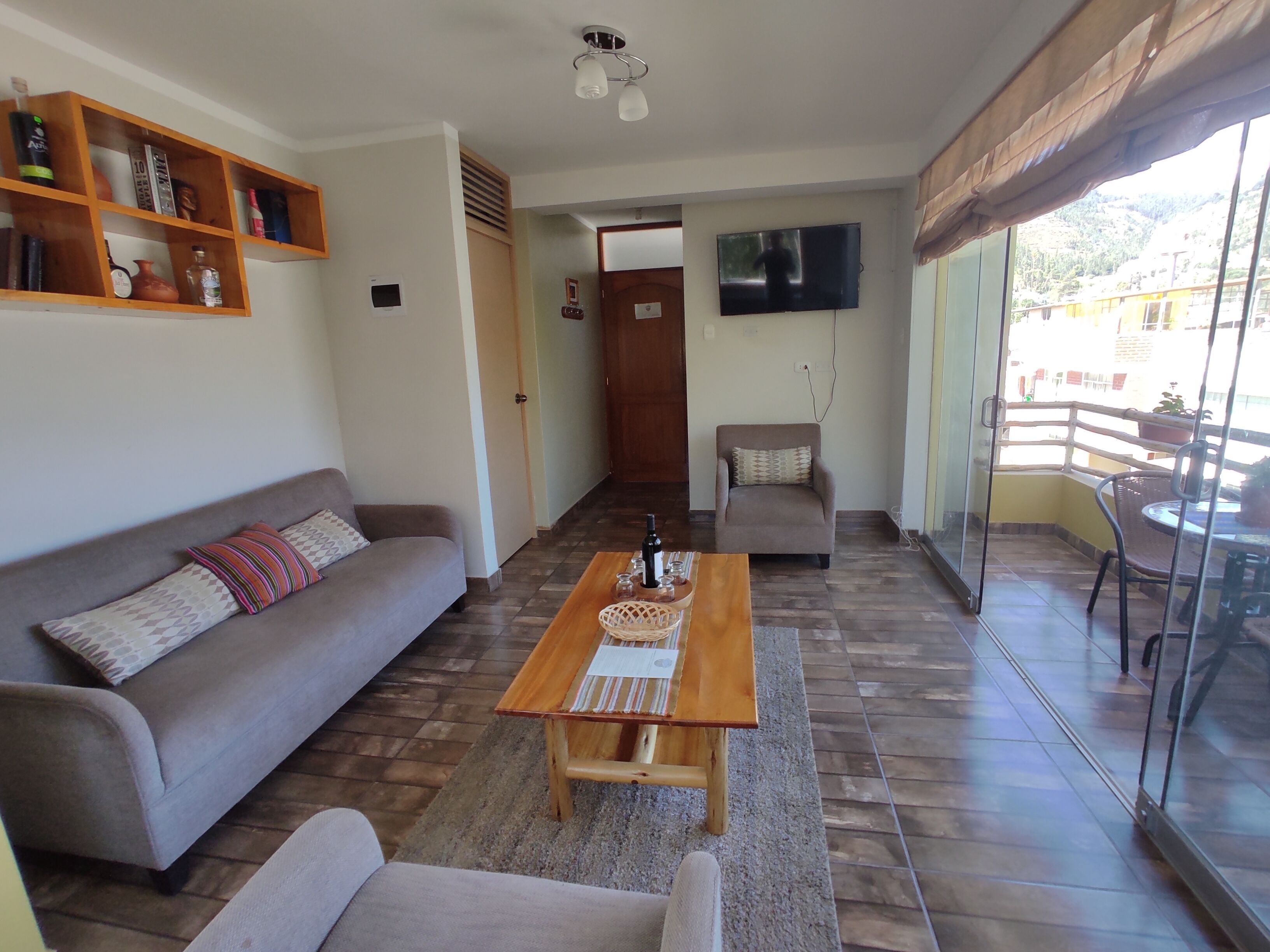 A living room with a sofa, a coffee table, a TV, and a balcony with a table and chairs.