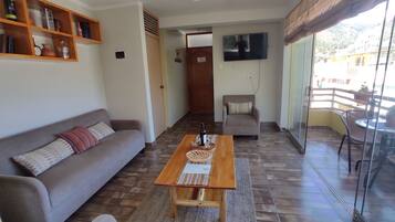 A living room with a sofa, a coffee table, a TV, and a balcony with a table and chairs.