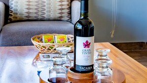Una mesa con una botella de vino Gran Tinto, copas, una cesta y un mando a distancia.