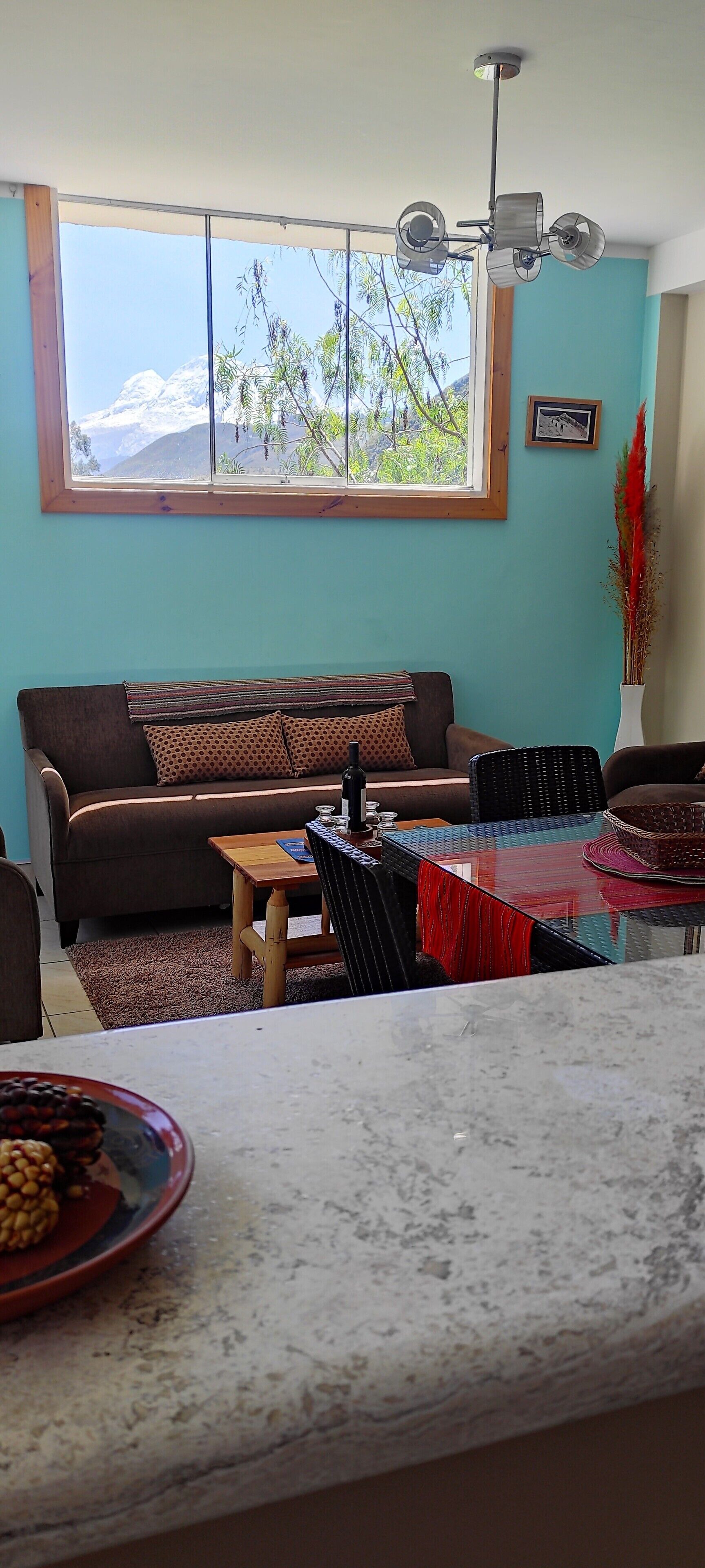 Sala de estar com sofá, mesa de jantar e vista para montanhas através de uma grande janela.